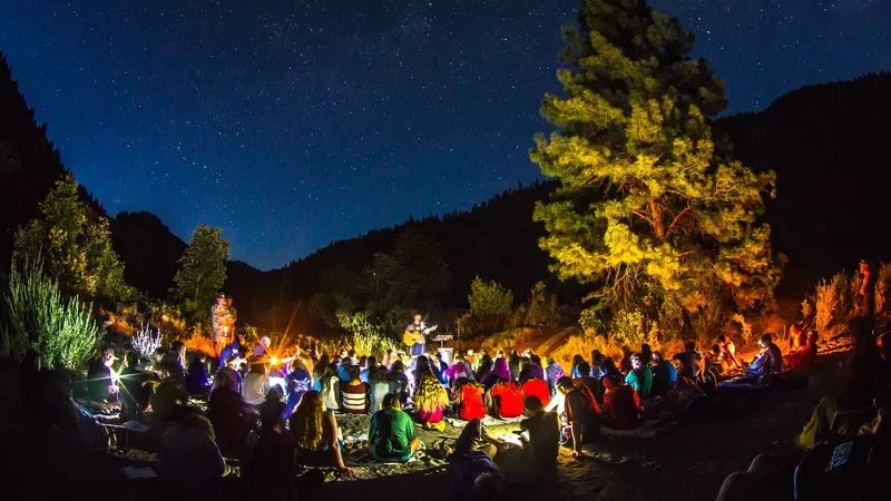 An audience gathered outdoors to listen to a man playing a guitar.